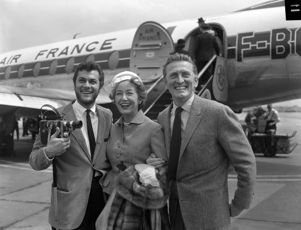 Hollywood film star Kirk Douglas and his wife Anne Buydens being met by Tony Curtis, left, on their arrival at London Airport from Paris. (Photo credit: PA Wire) 