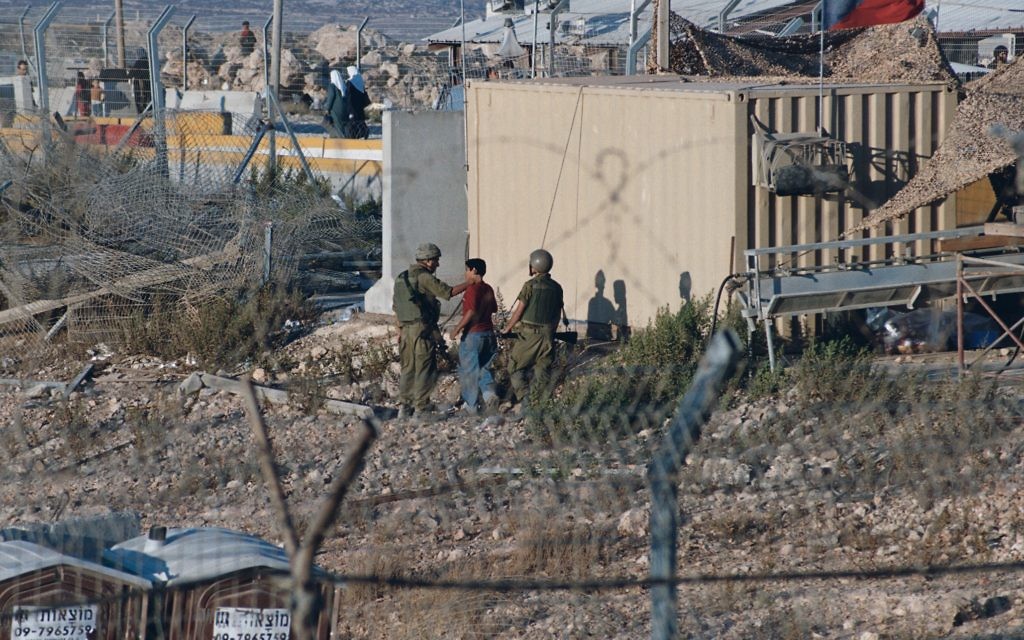 Israeli soldiers at Kalandia checkpoint in occupied West Bank taking Palestinian minors out of sight behind a building and assaulting them (presumably in an effort to obtain information from them). Other soldiers interrupted my photo-taking as the pictured soldiers repeatedly struck the kid in the head.