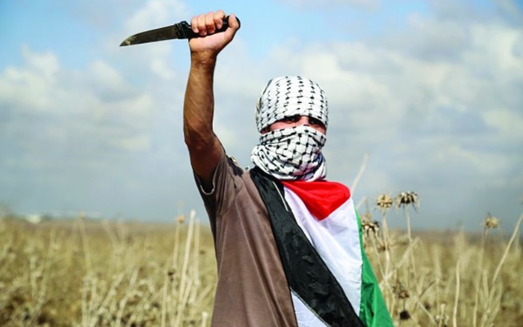 A Palestinian protester, holding a knife, looks on during clashes with Israeli security forces near the border fence between Israel and the Gaza Strip