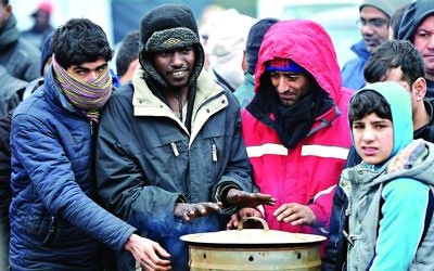 Migrants warm their hands at “the Jungle” camp in Calais