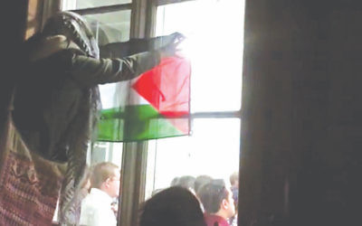 An anti-Israel protester waves a Palestinian flag through the window of the event at KLC with an Israeli speaker