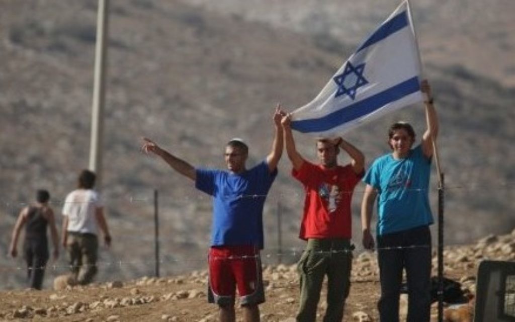 Jewish settlers hold an Israeli flag after they put up a fence in the West Bank village of Khirbet Ein al-Hilweh, in the Jordan Valley. (AP Photo/Nasser Ishtayeh, File)