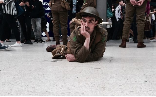 An actor on the Waterloo station platform floor, as part of the 'We are here' project