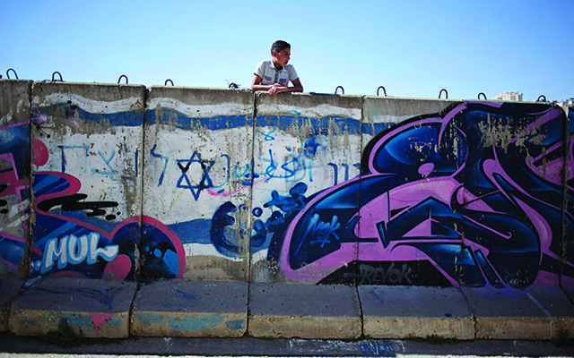 A Palestinian boy looks behind a wall separating Jewish part and Palestinian part of the West Bank