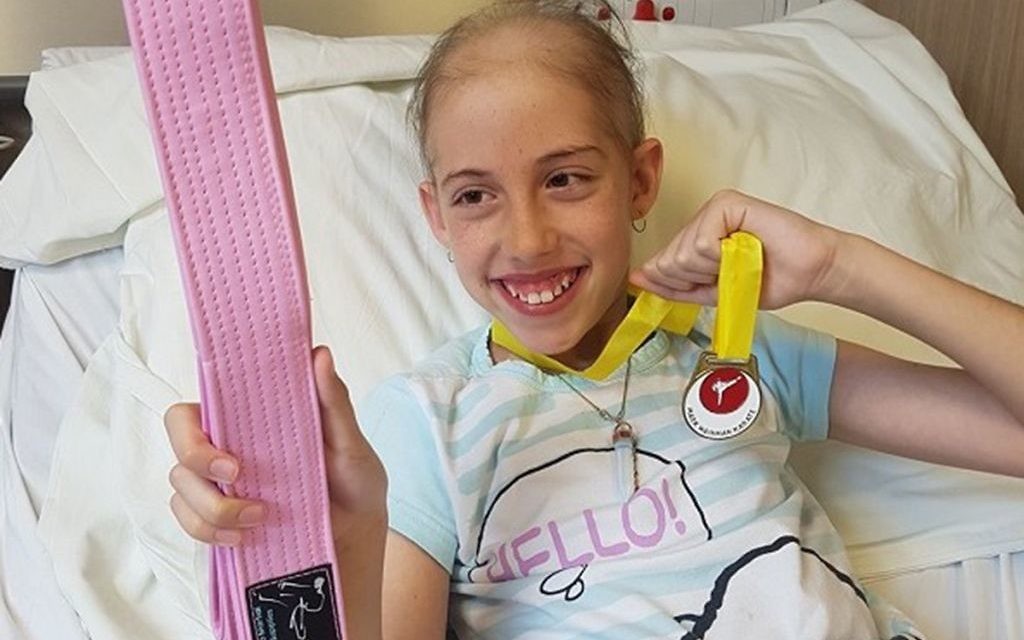 Hannah Katz with a pink karate belt in hospital, fighting but in good spirits
