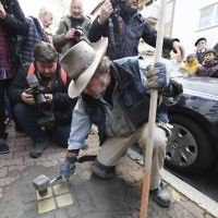 Artist Gunter Demnig lays four "Stolpersteine" (stumbling blocks) for Karolina Cohn and her family in Frankfurt, Germany, Monday, Nov. 13, 2017. Relatives participated in a memorial ceremony for Karolina Cohn, a Jewish girl from Frankfurt who perished in the Holocaust more than 70 years ago. The story of her life and death had been all but erased by the Nazis, until archeologists last year unearthed a silver pendant engraved with her birth date and birthplace at the grounds of the former Sobibor death camp. (Arne Dedert/dpa via AP)