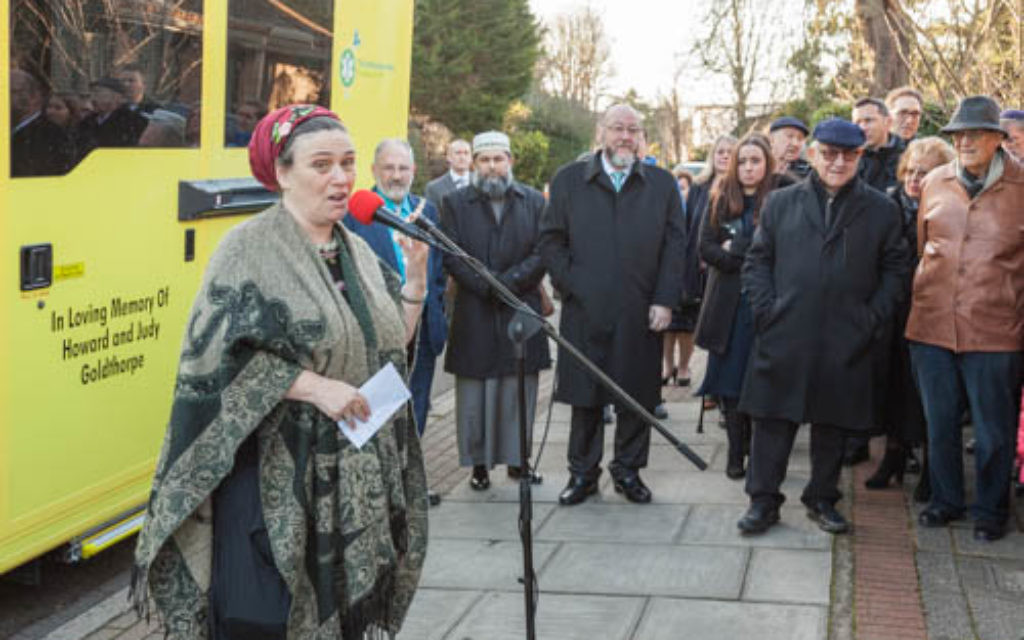 Skydiving rebbetzin Freda Kaplan speaking to a crowd including the Chief Rabbi, as the Wish Ambulance is presented