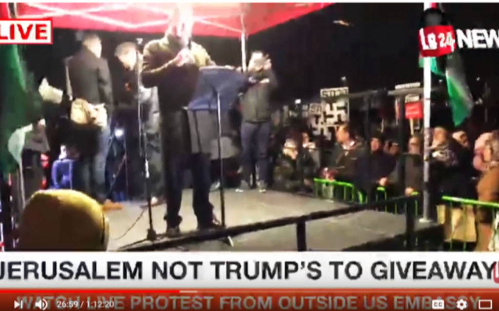 Swastikas can be seen in the background of the video, as a speaker addresses the demonstration