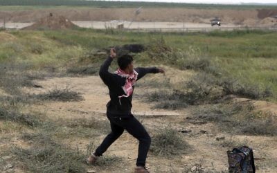 A Palestinian protester hurls stones toward Israeli soldiers during a demonstration near the Gaza Strip border with Israel, in eastern Gaza City, Friday, March 30, 2018. (AP Photo/ Khalil Hamra)