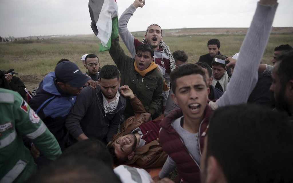 Palestinian protesters carry a wounded man was shot by Israeli troops during a demonstration near the Gaza Strip border with Israel, in eastern Gaza City, Friday, March 30, 2018. (AP Photo/ Khalil Hamra)