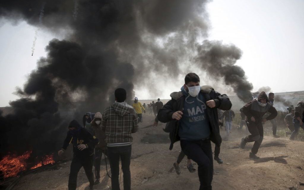 Palestinian protesters run for cover from teargas fired by Israeli troops during a protest at the Gaza Strip's border with Israel, Friday, April 6, 2018. (AP Photo/ Khalil Hamra)