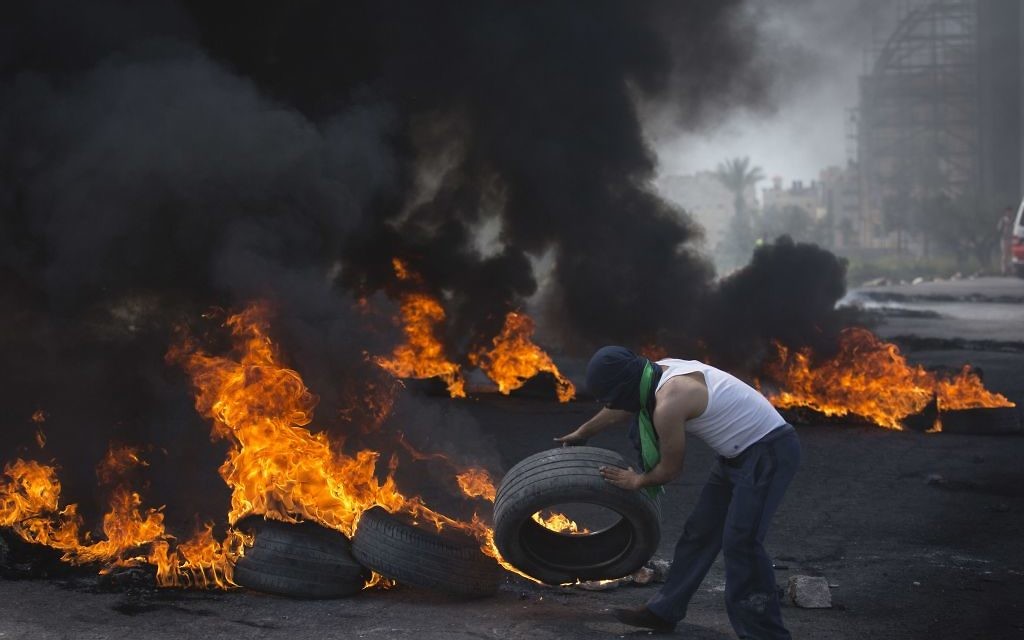 A Palestinian protester throws a tire into a pile of burning tires during clashes with Israeli border police, in the West Bank city of Ramallah, Friday, April 6, 2018. (AP Photo/Nasser Nasser)