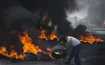 A Palestinian protester throws a tire into a pile of burning tires during clashes with Israeli border police, in the West Bank city of Ramallah, Friday, April 6, 2018. (AP Photo/Nasser Nasser)