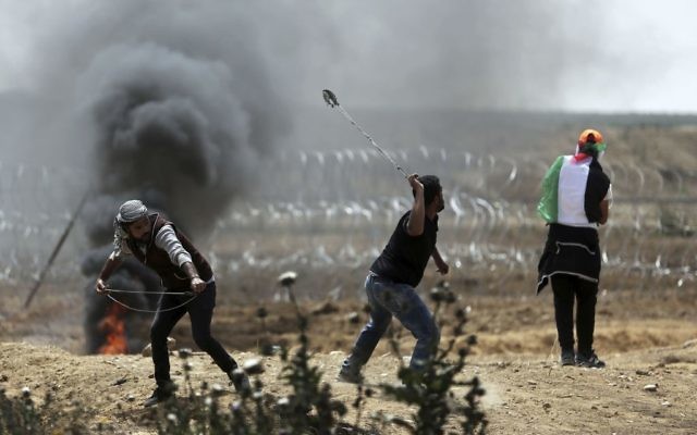 Palestinian protesters hurl stones at Israeli troops during a protest at the Gaza Strip's border with Israel, Friday, April 13, 2018. (AP Photo/ Khalil Hamra)