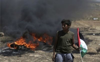 A boy holds a Palestinian flag in front of burning tires during a protest at the Gaza Strip's border with Israel, Monday, May 14, 2018.  (AP Photo/Khalil Hamra)