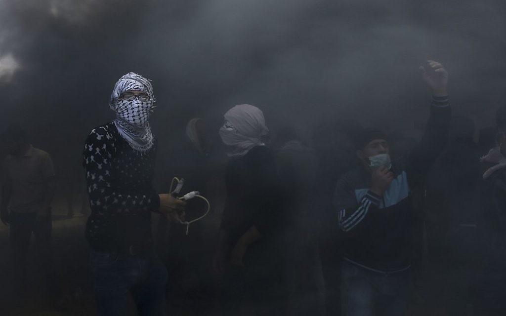Palestinian protesters hurl stones at Israeli troops while engulfed in smoke from burning tires near the Gaza Strip's border with Israel, east of Khan Younis, in the Gaza Strip, Monday, May 14, 2018.  (AP Photo/Adel Hana)