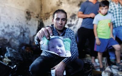 A relative holds up a photo of a one-and-a-half year old boy, Ali Dawabsheh, in a house that had been torched in a suspected attack by Jewish settlers in Duma village near the West Bank city of Nablus, Friday, July 31, 2015. T (AP Photo/Majdi Mohammed)