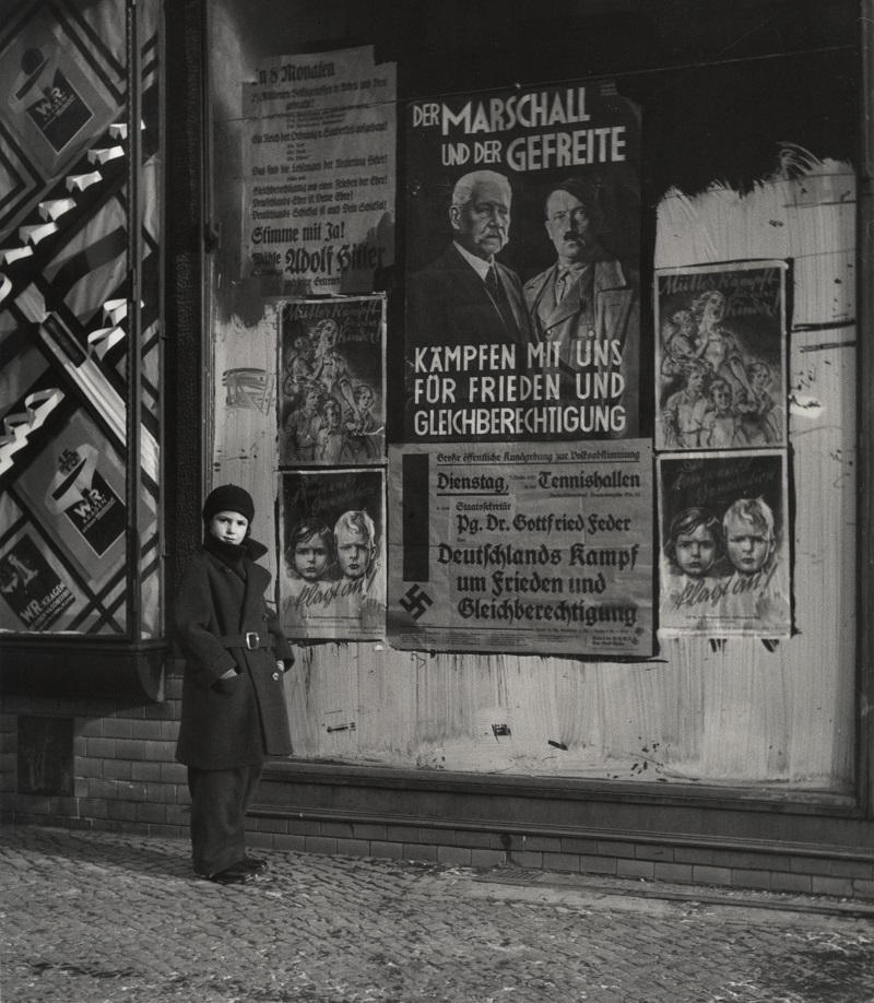 Vishniac’s daughter, Mara, posing in front of an election poster for Hindenburg and Hitler that reads “The Marshal and the Corporal: Fight with Us for Peace and Equal Rights”, Berlin, 1933. Credit: Mara Vishniac Kohn