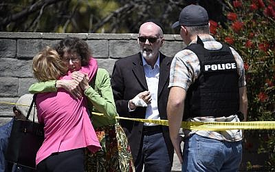 Two people hug as another talks to a San Diego County Sheriff's deputy outside of the Chabad of Poway Synagogue, following the deadly attack in April 2019, in Poway, Calif. (AP Photo/Denis Poroy)