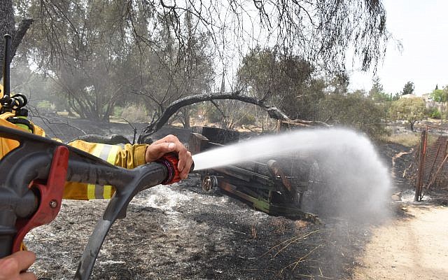 An Israeli firefighter sprays water on an agricultural machinery destroyed following a fire amidst extreme heat wave in the village of Mevo Modi'im, in central Israel on May 24, 2019. Photo by: JINIPIX