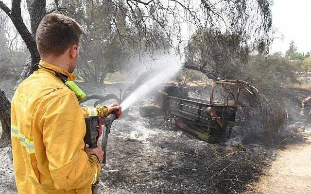 An Israeli firefighter sprays water on an agricultural machinery destroyed following a fire amidst extreme heat wave in the village of Mevo Modi'im, in central Israel on May 24, 2019. Photo by: JINIPIX