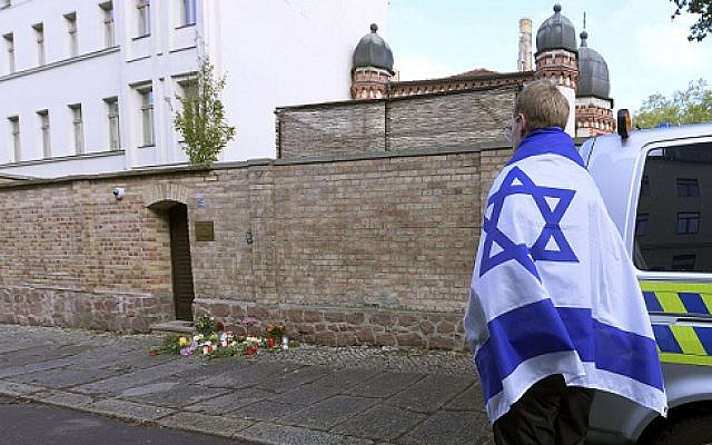 A person with a flag of Israel stands next to flowers and candles in front of a synagogue in Halle, Germany, following a terror shooting on Yom Kippur in 2019 (AP Photo/Jens Meyer via Jewish News)