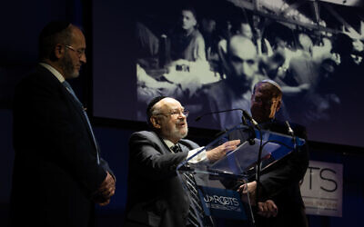 Holocaust Survivor Josef Lewkowicz stood next to a photograph of himself in Ebensee camp, with Tzvi Sperber and Rabbi Naftali Schiff
 (Credit: Blake Ezra Photography)