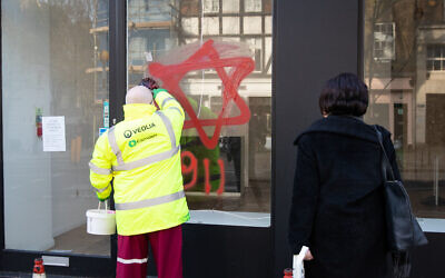 A council cleaner removes anti-semitic graffiti in the form of numbers, 9 11, and a Star of David, on a shop window in Belsize Park, North London. ( Photo credit: Aaron Chown/PA Wire_