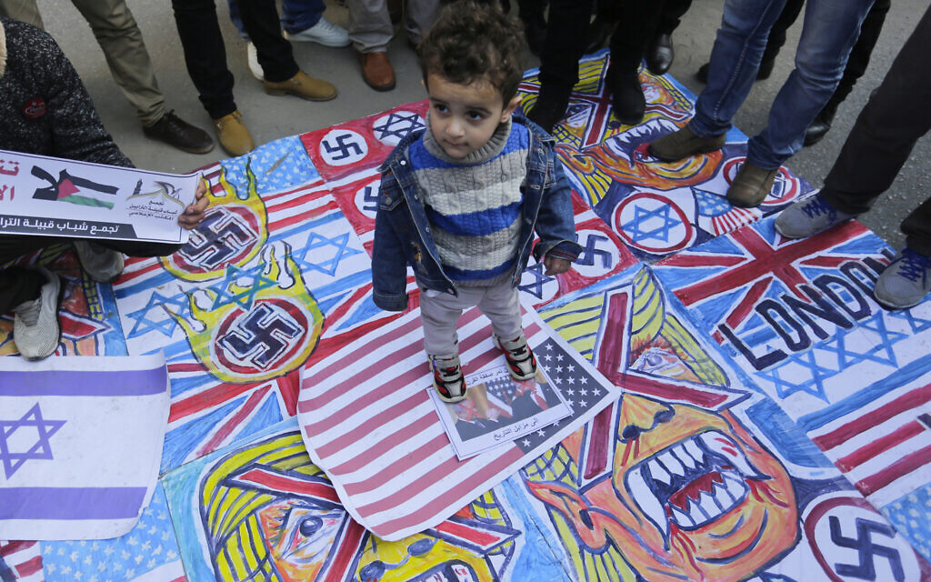 A Palestinian child stands on the illustrations of the British Union flag, the Israeli flag, and an American flag during a protest against the American peace plan in the Middle East, in Gaza City. (Photo by Mahmoud Issa / SOPA Images/Sipa USA)