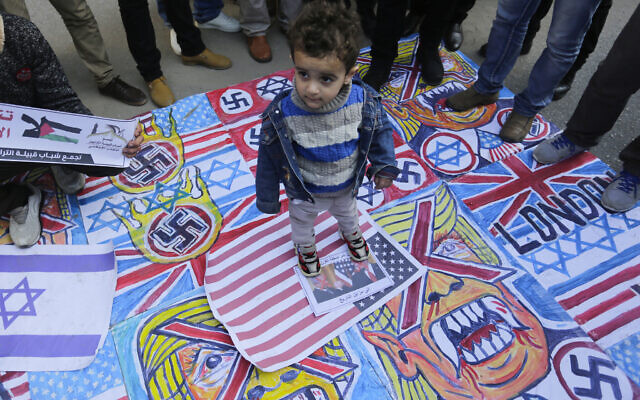 A Palestinian child stands on the illustrations of the British Union flag, the Israeli flag, and an American flag during a protest against the American peace plan in the Middle East, in Gaza City. (Photo by Mahmoud Issa / SOPA Images/Sipa USA)