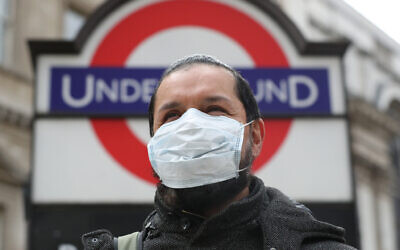 A person wearing a face mask in front of an underground sign in London.