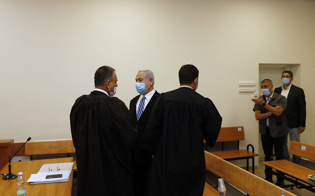 Israeli Prime Minister Benjamin Netanyahu, wearing a face mask in line with public health restrictions due to the coronavirus pandemic, center, stands inside the court room with his lawyers  as his corruption trial opens at the Jerusalem District Court, Sunday, May 24, 2020.  He is the countryÕs first sitting prime minister ever to go on trial, facing charges of fraud, breach of trust, and accepting bribes in a series of corruption cases stemming from ties to wealthy friends. (Ronen Zvulun/ Pool Photo via AP)