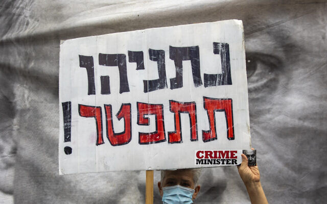 A protester against Israel's Prime Minister Benjamin Netanyahu holds a placard that reads, "Netanyahu resign," during a protest outside his residence in Jerusalem, Sunday, May 24, 2020.   (AP Photo/Ariel Schalit)