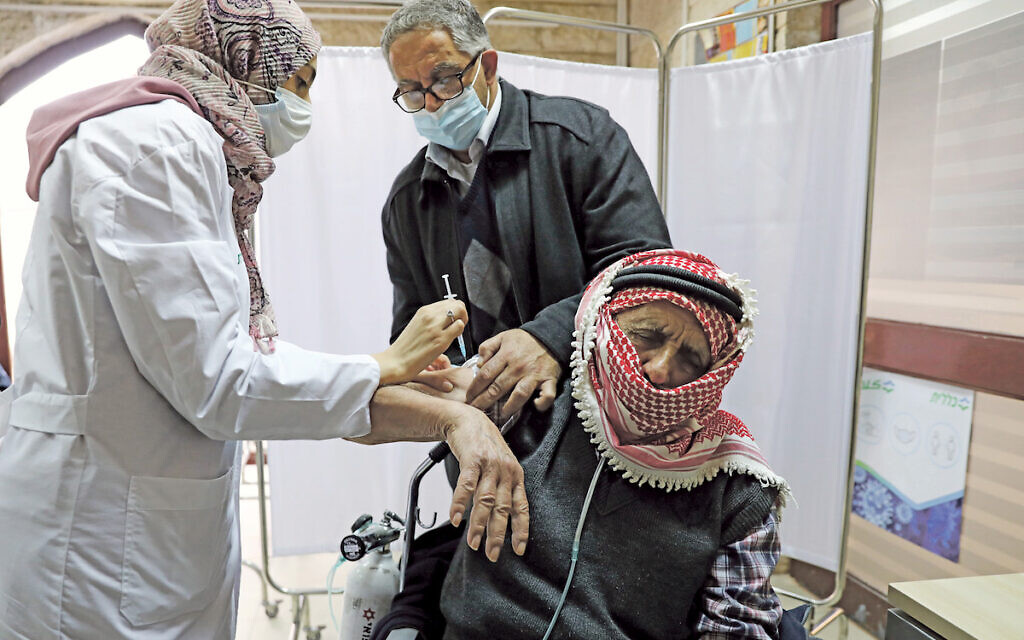 A Palestinian man is helped by his son as he receives a vaccination against the coronavirus disease (COVID-19) as Israel continues its national vaccination drive, in East Jerusalem December 23, 2020. REUTERS/Ammar Awad