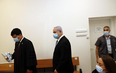 Israeli Prime Minister Benjamin Netanyahu, center, wearing a face mask in line with public health restrictions due to the coronavirus pandemic, enters the court room with his lawyer as his corruption trial opens at the Jerusalem District Court