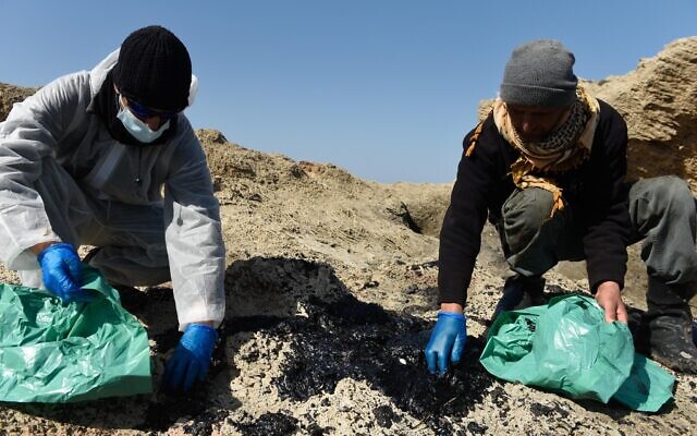 Israelis clean tar from the sand after an offshore oil spill drenched much of Israel's Mediterranean shoreline, at a beach in Atlit, Israel February 22, 2021. Photo by: Roni Ofer-JINIPIX