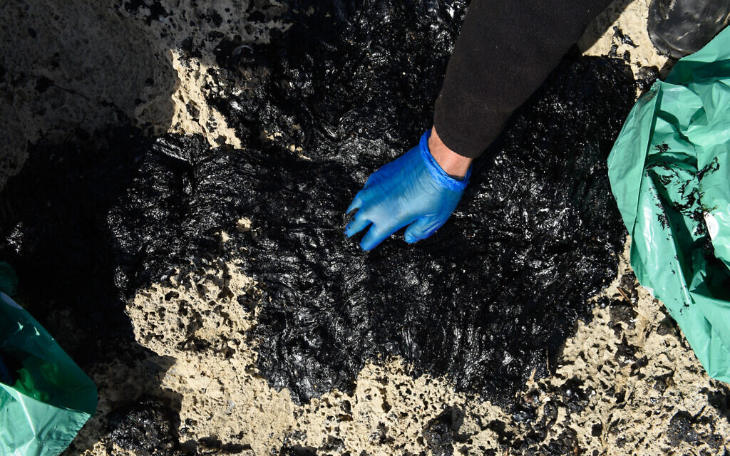 Israelis clean tar from the sand after an offshore oil spill drenched much of Israel's Mediterranean shoreline, at a beach in Atlit, Israel February 22, 2021. Photo by: Roni Ofer-JINIPIX
