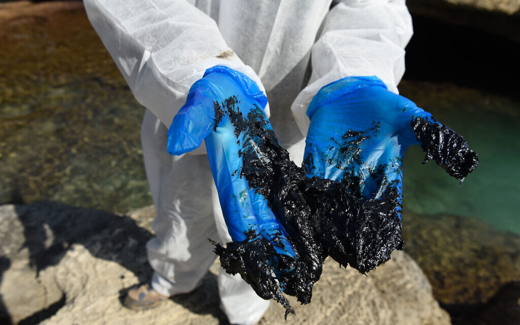 Israelis clean tar from the sand after an offshore oil spill drenched much of Israel's Mediterranean shoreline, at a beach in Atlit, Israel February 22, 2021. Photo by: Roni Ofer-JINIPIX