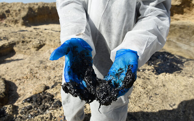 Israelis clean tar from the sand after an offshore oil spill drenched much of Israel's Mediterranean shoreline, at a beach in Atlit, Israel February 22, 2021. Photo by: Roni Ofer-JINIPIX