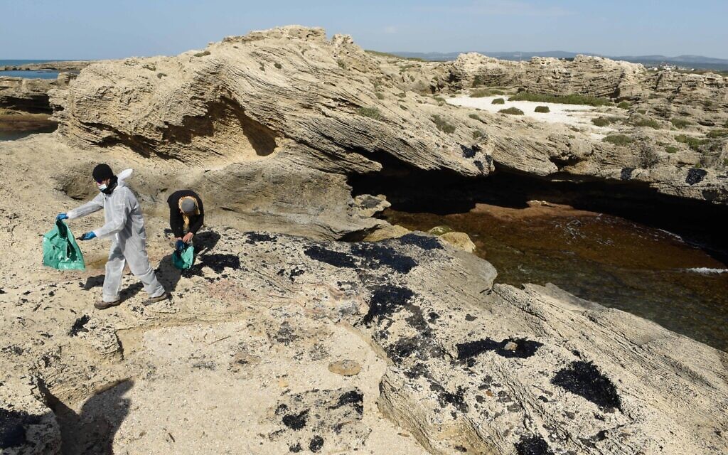 Israelis clean tar from the sand after an offshore oil spill drenched much of Israel's Mediterranean shoreline, at a beach in Atlit, Israel February 22, 2021. Photo by: Roni Ofer-JINIPIX