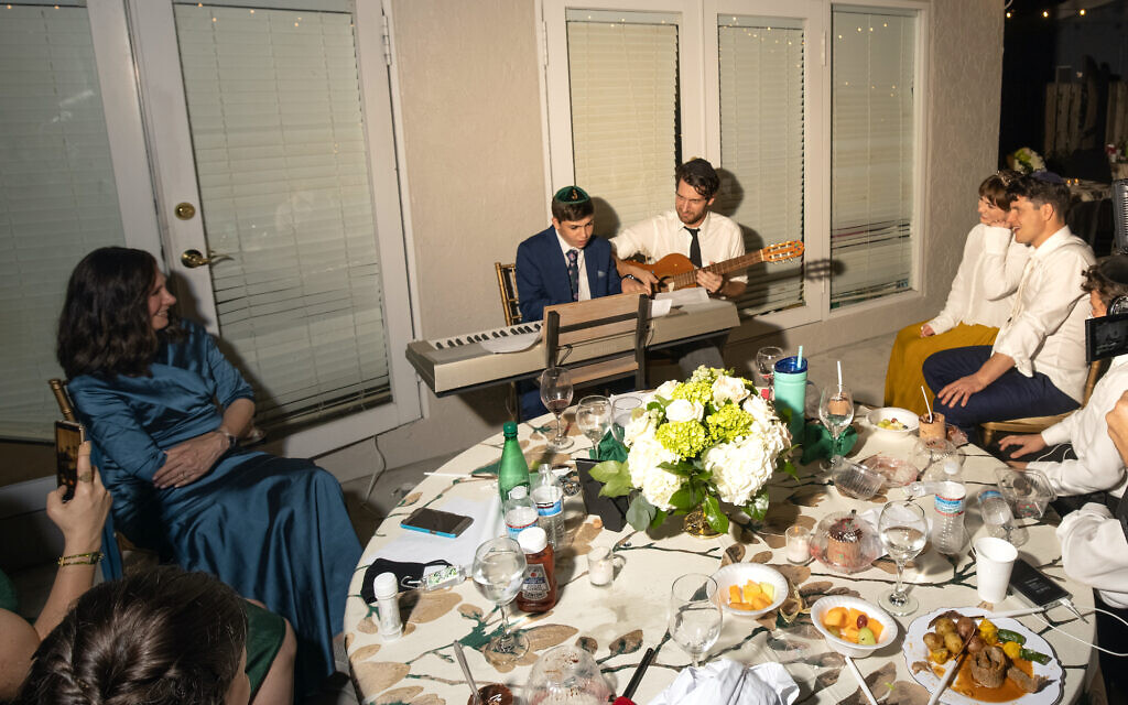 Judy Kaiser (left) and her son Menachem Kaiser (holding the guitar next to his nephew) pictured together at his brother's wedding. Author Menachem has received date offers after his mother announced "he's single" to an online conference with a synagogue about his new book.