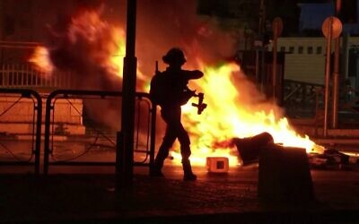 An Israeli officer stands in front of a fire burning in the street in Jerusalem on Thursday night (Photo: Reuters)