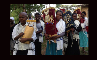 Women and children carry Torah scrolls from an old synagogue building to a new building in Nabagoye, Uganda. (Courtesy of Be’chol Lashon) Via JTA