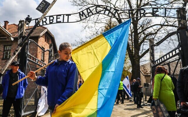 A Ukrainian refugee from Vinnytsia, is seen holding Ukrainian flag in front of the entrance gate with 'Arbeit Macht Frei' inscription during March of the Living.
