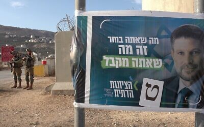 2K81PPW WEST BANK - OCTOBER 19: Israeli soldiers stand next to an election campaign banner for the far right Religious Zionism party (HaZionut HaDatit) depicting its leader Bezalel Smotrich with a caption reading, ?What you choose is what you get" hanged at the military Awarta checkpoint one of several checkpoints that surround the Palestinian city of Nablus on October 19, 2022 in Nablus, West Bank. Credit: Eddie Gerald/Alamy Live News