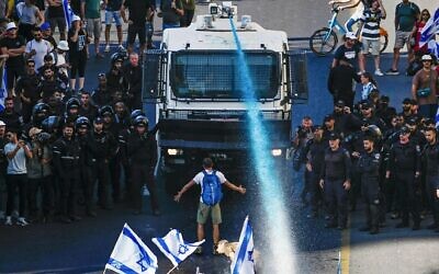 A person stands in front of an Israeli police water cannon being used to disperse demonstrators blocking a road during a protest against plans by Prime Minister Benjamin Netanyahu's government to overhaul the judicial system, in Jerusalem, Monday, July 24, 2023. (AP Photo/Ariel Schalit)