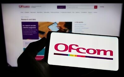 Person holding mobile phone with logo of UK authority Office of Communications (Ofcom) on screen in front of web page.