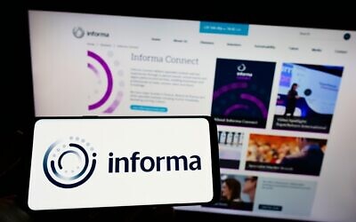 Person holding cellphone with logo of British publishing company Informa plc on screen in front of business webpage. Focus on phone display.