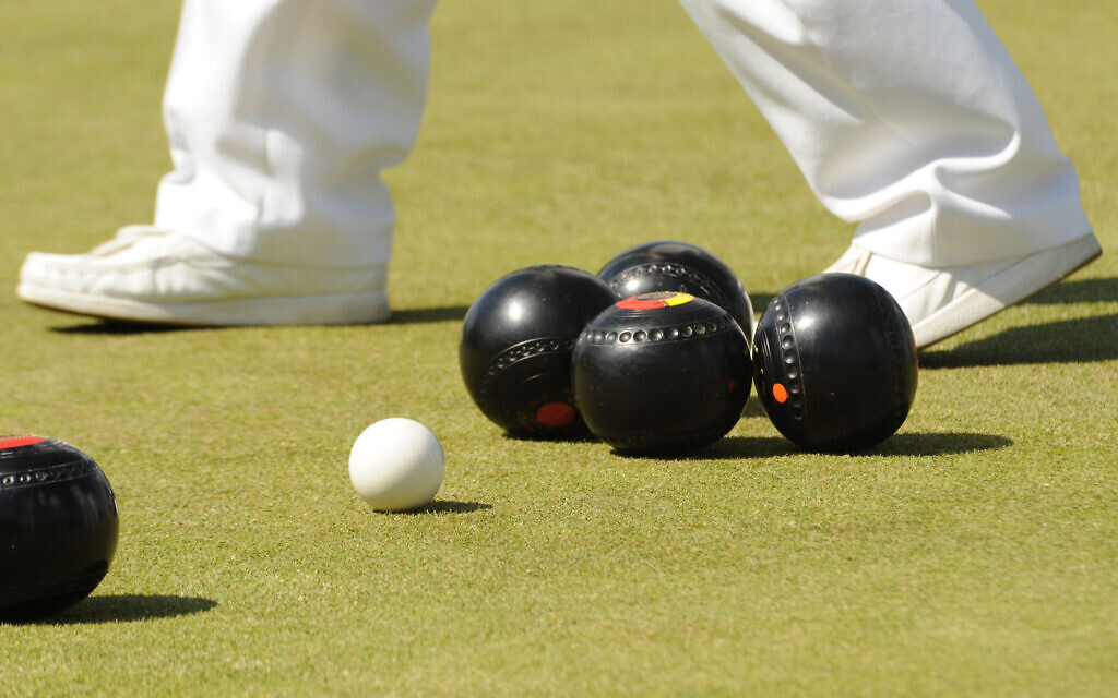 A photograph of lawn bowls with a players feet in the background