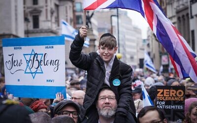 A young Jewish boy sits on his fathers shoulders waving a British Union flag.